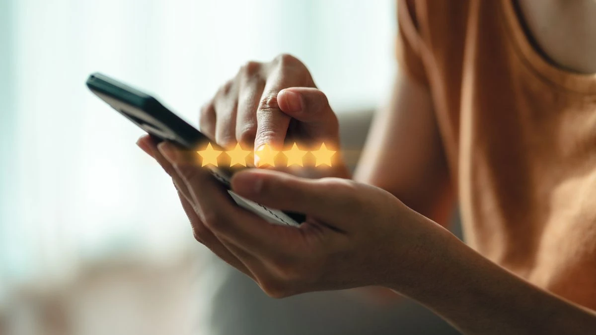 7 estratégias de fidelização para pequenos negócios Pessoa utilizando um smartphone, interagindo com a tela enquanto avalia um aplicativo com estrelas de rating visíveis.
